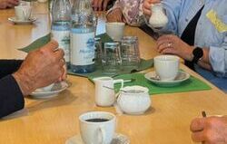 Man sieht eine gedeckte Kaffeetaffel, an der mehrere Personen sitzen und gerade Kaffee trinken.